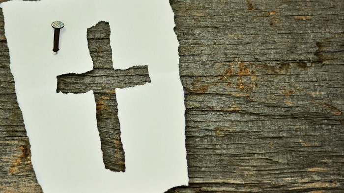 Ein Nagel und ein Kreuz auf einem Baumstamm.