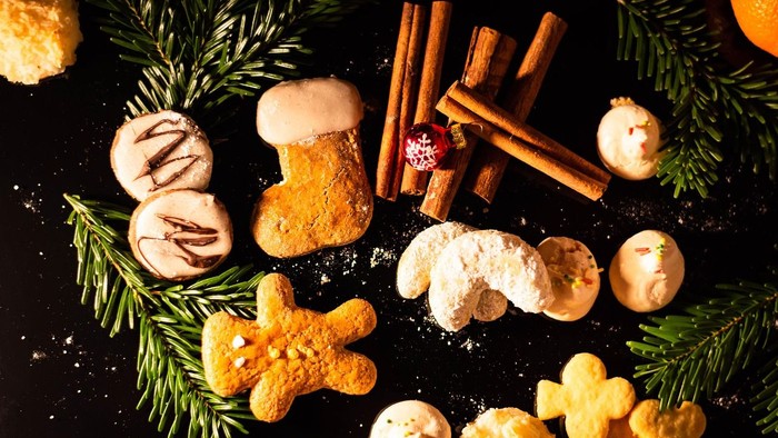 Weihnachtsplätzchen, Zimtstangen und Tannenzweige auf schwarzem Hintergrund