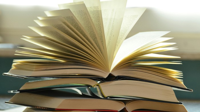 Ein Stapel Bücher, wobei das oberste Buch aufgeschlagen ist und Sonnenlicht einfängt