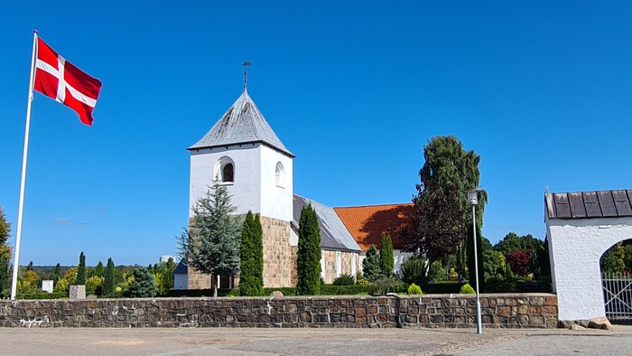 En kirke med tårn og en dansk flag på en klar dag