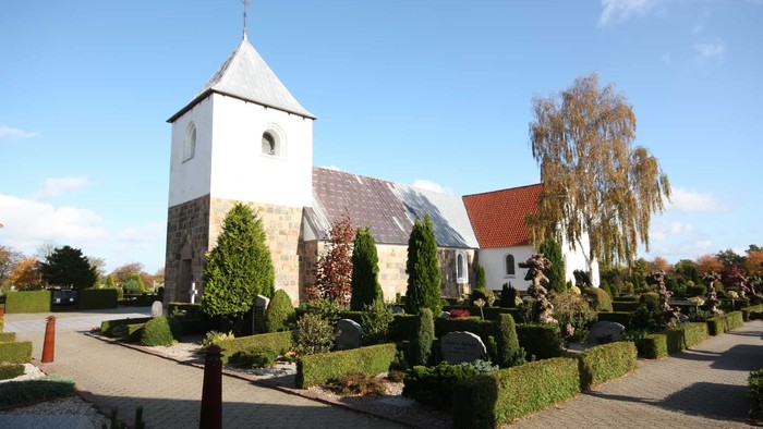 En lille kirke med klokketårn og en have med høje buske og træer