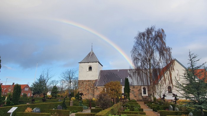 En regnbue over en kirke med en have foran