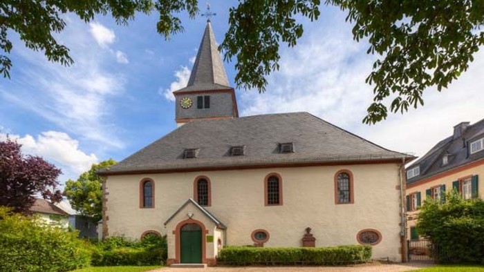 Idyllische Kirche mit hohem Kirchturm, umgeben von üppigem Grün und einem ruhigen Innenhof.