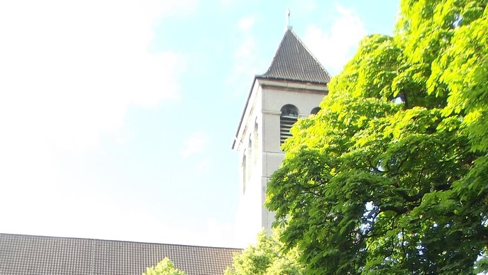 Menschen sitzen im Freien vor einem Gebäude mit Kirchturm.