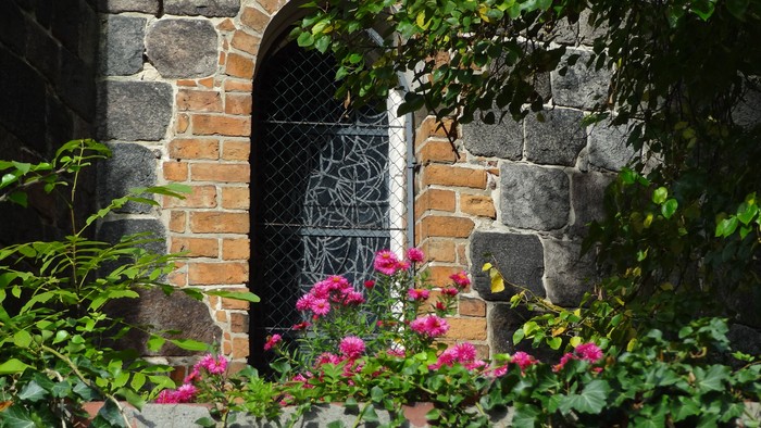 Ein Blumenbeet mit rosa Blumen vor einer Steingruppe mit Metalltür