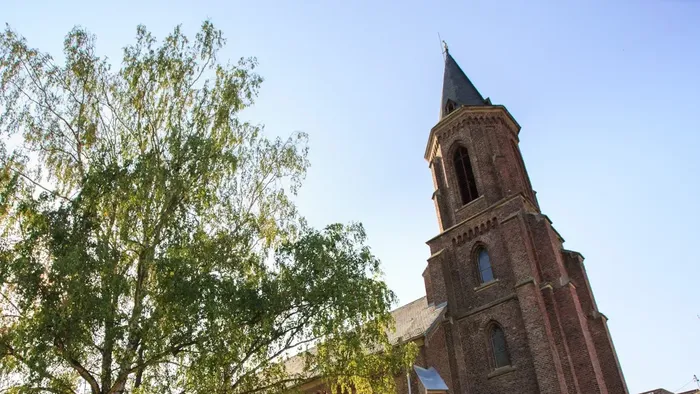 Historische Backsteinkirche mit hohem Turm, umgeben von üppigem Grün unter klarem Himmel.