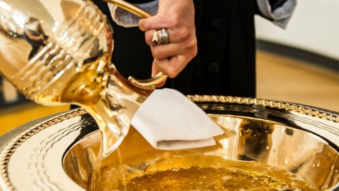 En person hælder væske fra en gylden kalk ind i et fad under en ceremoniel ritual.