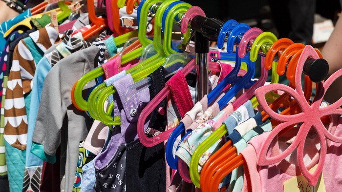 Bunte Kleiderbügel präsentieren verschiedene Kinderkleidung auf einem Markt oder Flohmarkt im Freien.