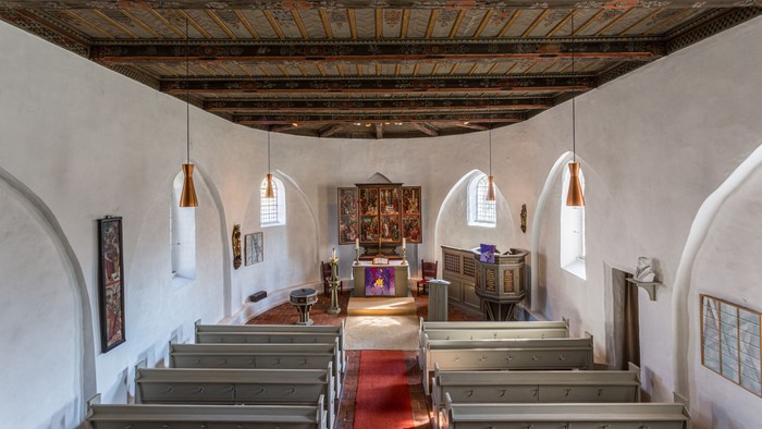 Historisches Kircheninneres mit hölzernen Kirchenbänken, prunkvoller Decke und traditionellem Altarschmuck.