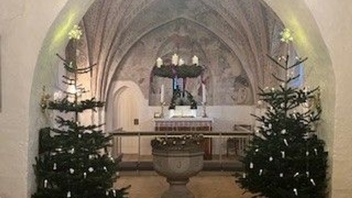 Udsmykkede juletræer flankerer en dåbsfont i et stort, hvælvet kirkerum.