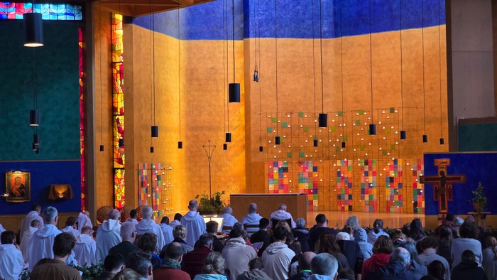 Eine überfüllte Kirchenmesse mit lebhaften Buntglasverzierungen und Gläubigen, die einem prunkvollen Altar zugewandt sind.