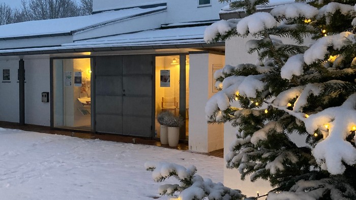 En hvid modern villa med store glaspane, beliggende i sneen med en juletree foran