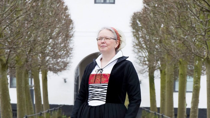 Kvinde i sort kjole med rød og hvid top, der står på en brostensbelagt sti.