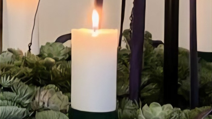 Elegant lysestagearrangement omgivet af frodig grønne planter og sukkulenter med en festlig, naturlig krans som baggrund.
