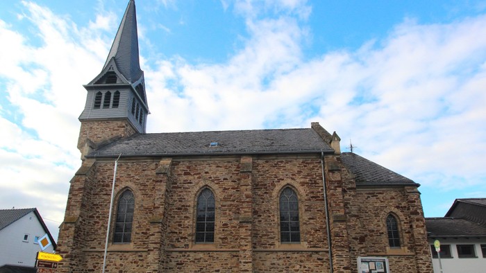 Historische Steinkirche mit hohem Kirchturm und Bogenfenstern unter einem teilweise bewölkten Himmel.