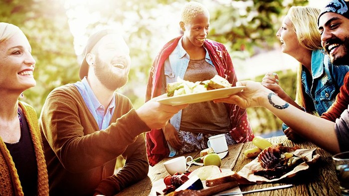 Fröhliche Menschen, die bei Sonnenschein gemeinsam im Freien essen.