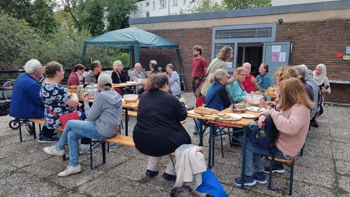 Eine Gruppe von Menschen sitzt im Freien an Tischen und isst.