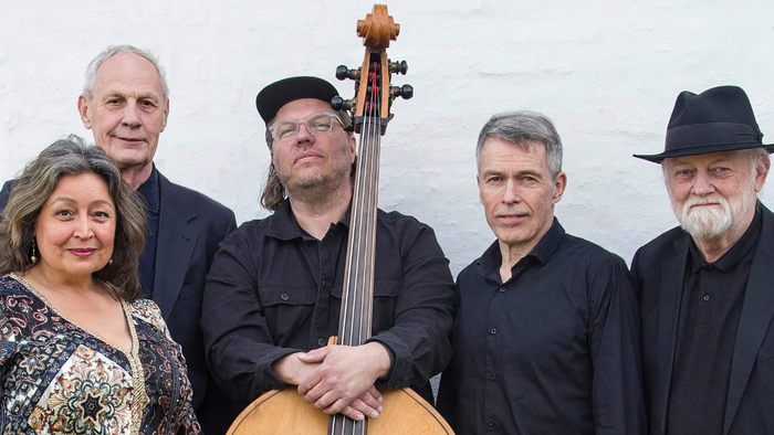En gruppe på fem musikere, der poser sammen, hvor én holder en cello.