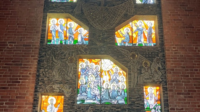 Buntglasfenster zeigen religiöse Szenen mit einem zentralen Kruzifix-Altar im Inneren einer Kirche.