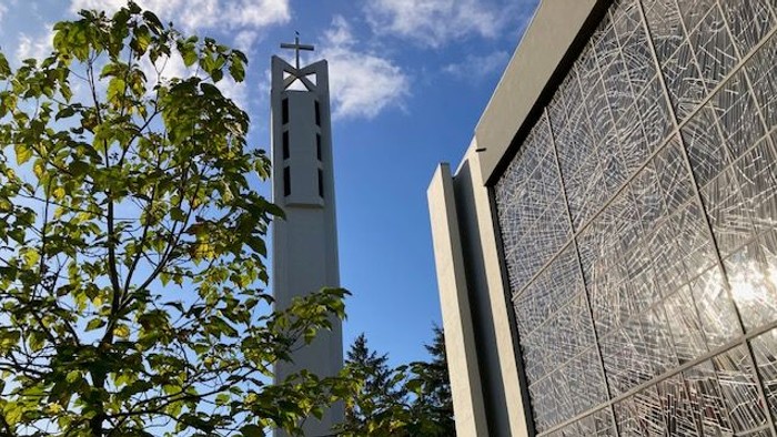 Moderne Kirche mit hohem Glockenturm und aufwendig gemusterter Fassade unter klarem blauem Himmel.