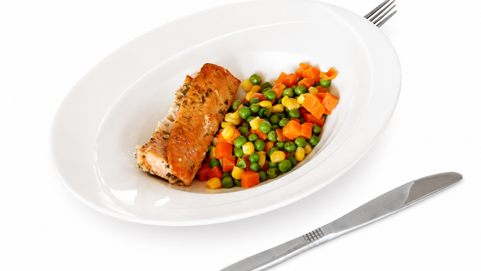 Lachs mit Gemüse auf einem Teller, daneben Besteck.