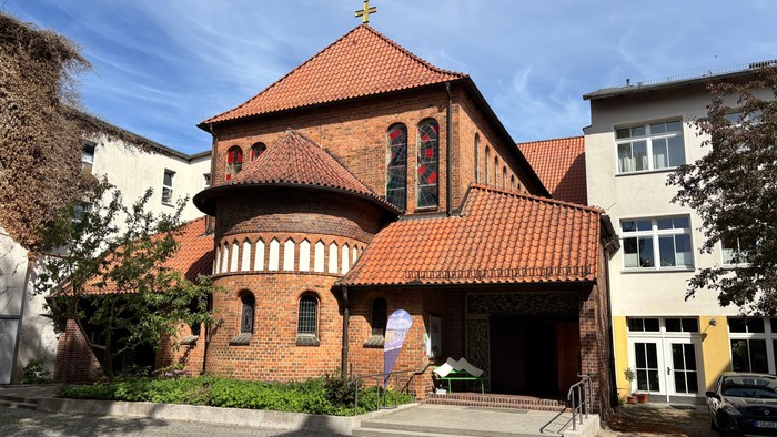 Historische Backsteinkirche mit rotem Ziegeldach und Bogenfenstern in einem malerischen städtischen Umfeld.