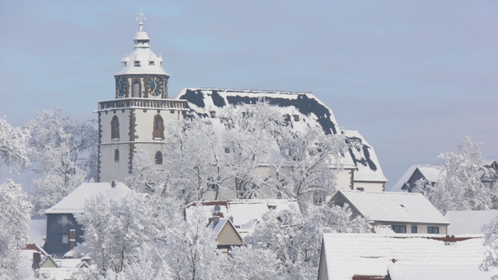 Schneebedeckte Gebäude und Bäume mit einem markanten Uhrturm im Hintergrund.