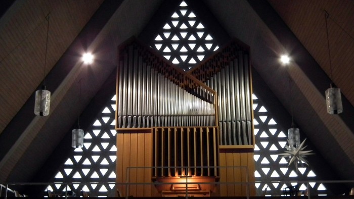 Kircheninneres mit großer Orgel und geometrischen Buntglasfenstern.