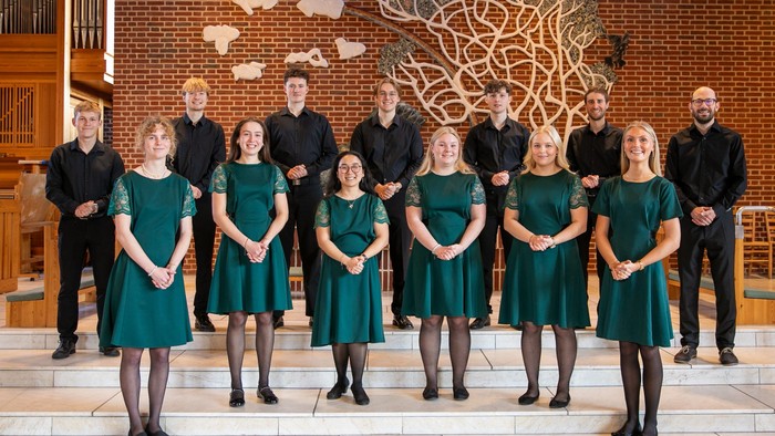 En kor med mænd og kvinder i grønne kider står i en kirke.