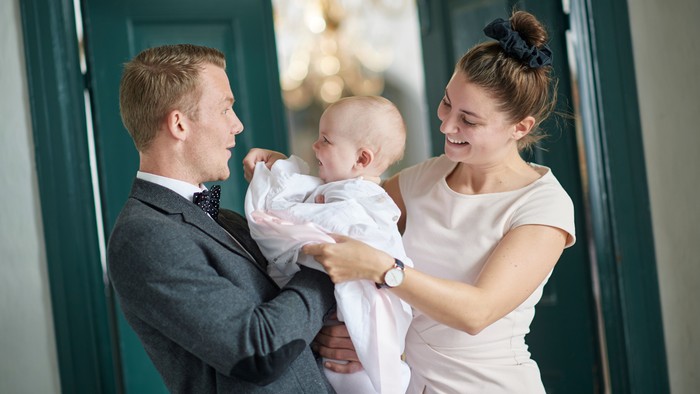 Et glædeligt par holder lykkeligt og smiler til deres nyfødte baby foran grønne døre.