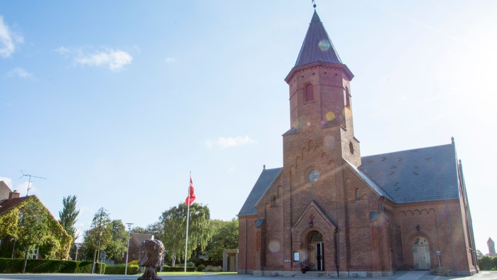 En rød kirke med tårn og en statue foran