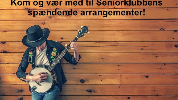 En mand med en cowboyhat spiller banjo foran en trævæg.