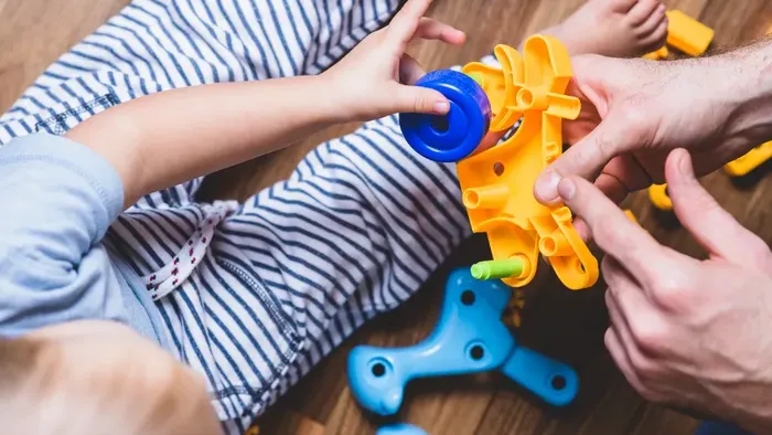 Kind und Erwachsener spielen mit bunten Plastikspielzeugen auf dem Boden.