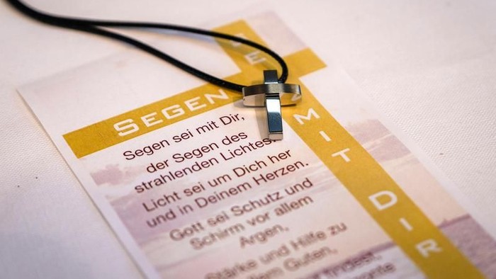Ein Kreuzanhänger liegt auf einem bedruckten Papier mit religiösem Text.