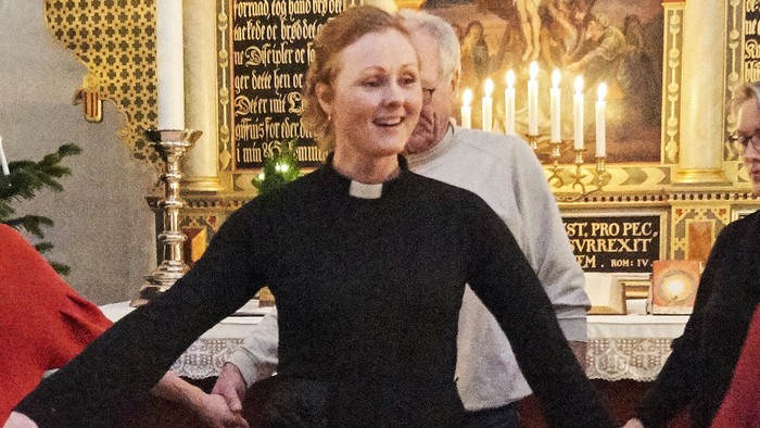 En præst og kirkegængere holder hinanden i hånden og danser