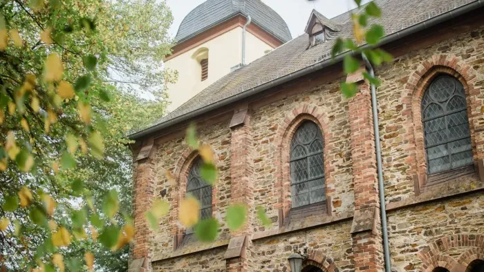 Historische Steinkirche mit Bogenfenstern und einem markanten Glockenturm, eingerahmt von Herbstlaub.