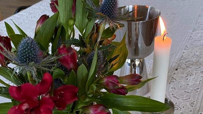 Blomster i en vase og stearinlys på en hvid blondedug.