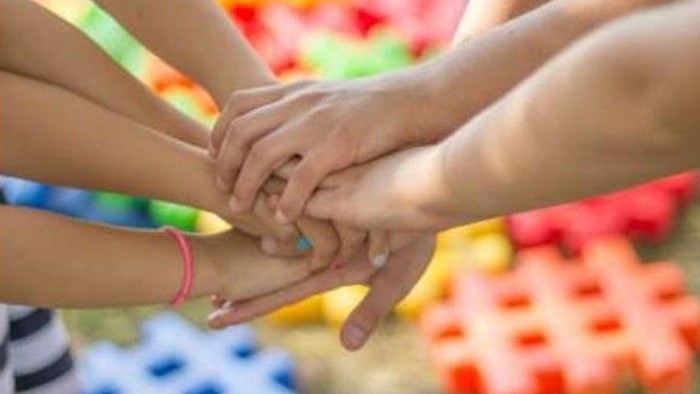 Mehrere Hände von jungen Menschen halten sich. Im Hintergrund bunte Bausteine.