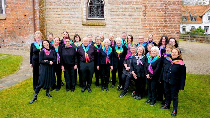 Gruppenfoto des Gospelchors aus März 2026. Die Chormitglieder stehen vor der Kirche und lächeln in die Kamera. Sie tragen einheitlich schwarze Kleidung und bunte Halstücher.