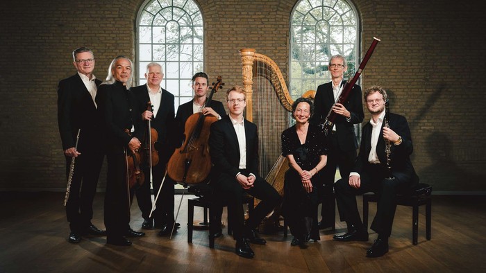 Et professionelt kammerensemble poserende med forskellige klassiske instrumenter i en elegant indendørs omgivelse.