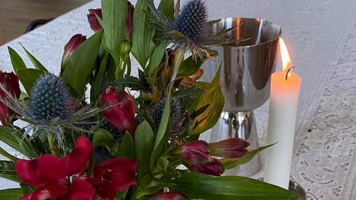 Blomster i en vase og stearinlys på en hvid blondedug.