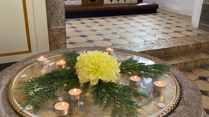 Elegant sten-dåbsfad prydet med lys, grønt og en lysende gul blomsterdekoration.