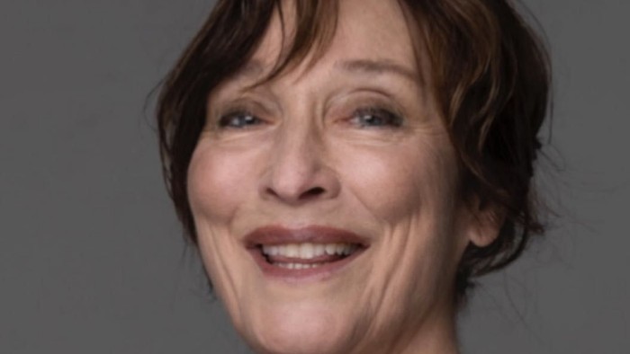 En smilende kvinde med kort hår i en mørk top poser mod en neutral baggrund.