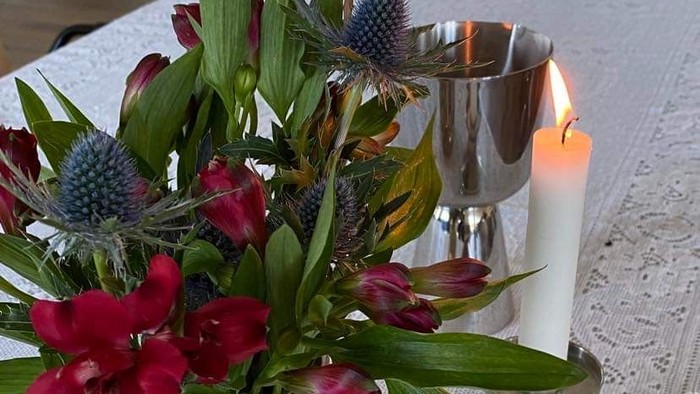 Blomster i en vase og stearinlys på en hvid blondedug.