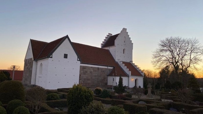 Historisk kirke badet i gyldent solnedgangslys med anlagt have og stenmure.