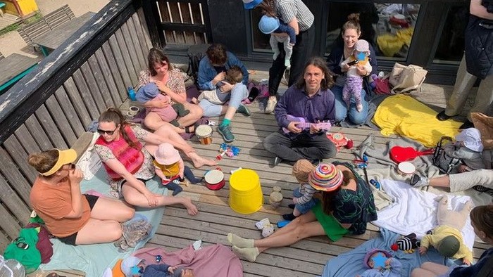 Et livligt udendørs arrangement med folk, der maler og slapper af på en terrasse med farverigt tøj og materialer.