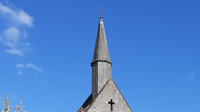 Kirche mit Wiese davor, blühendem Kirschbaum links und blauem Himmel