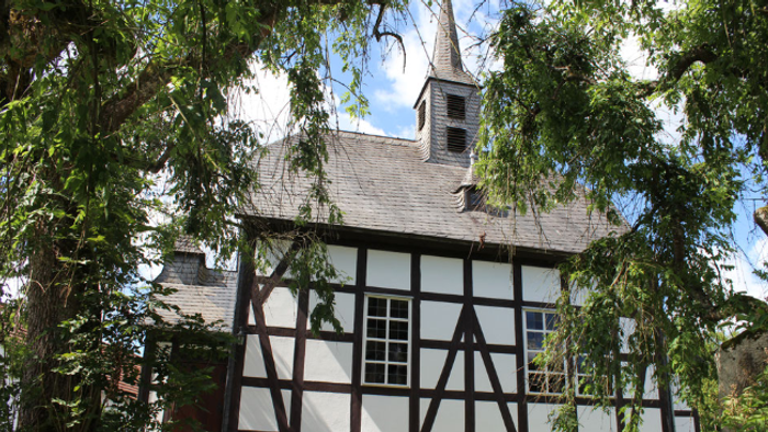 Historisches Gebäude mit Fachwerk, Steinsockel und Glockenturm.