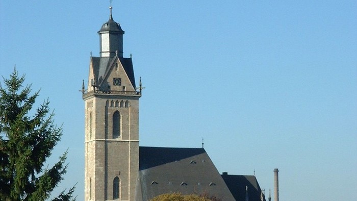 Der historische Kirchturm ragt über die malerischen, rotgedeckten Häuser eines europäischen Dorfes unter klarem blauem Himmel empor.