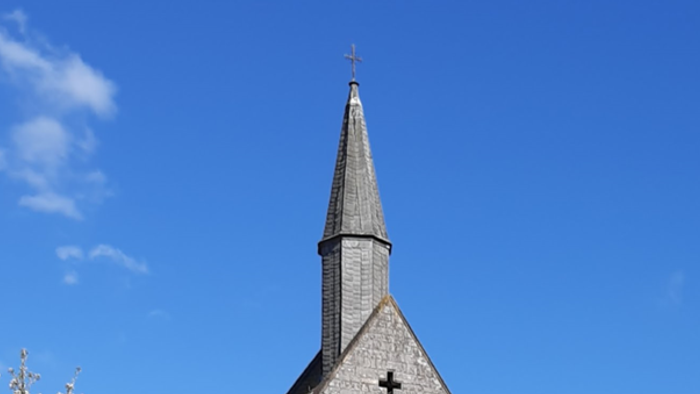 Kirche mit Wiese davor, blühendem Kirschbaum links und blauem Himmel